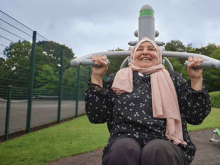 A woman wearing a head scarf uses a shoulder press machine in a park gym