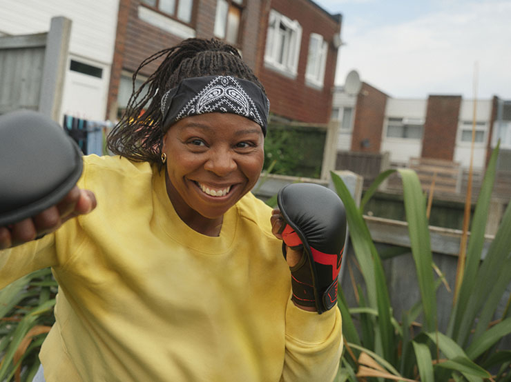 A woman shadow boxes using practice gloves in her back garden