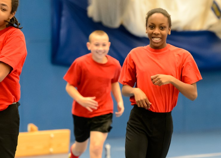 Boys and girls run around an indoors gym.