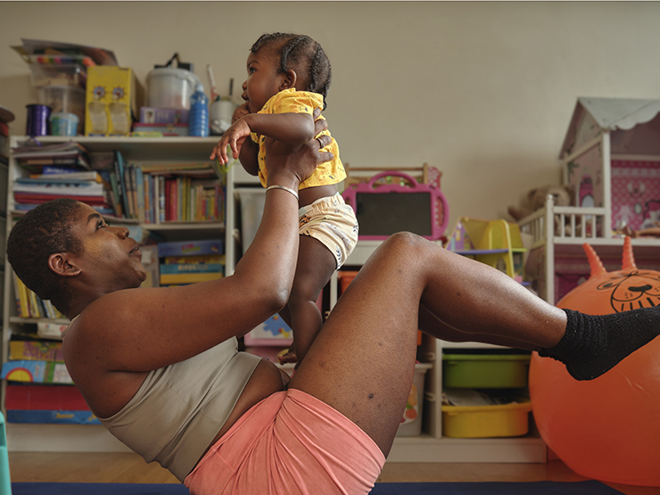 A Black woman performs crunches at home, while holding her baby in the air