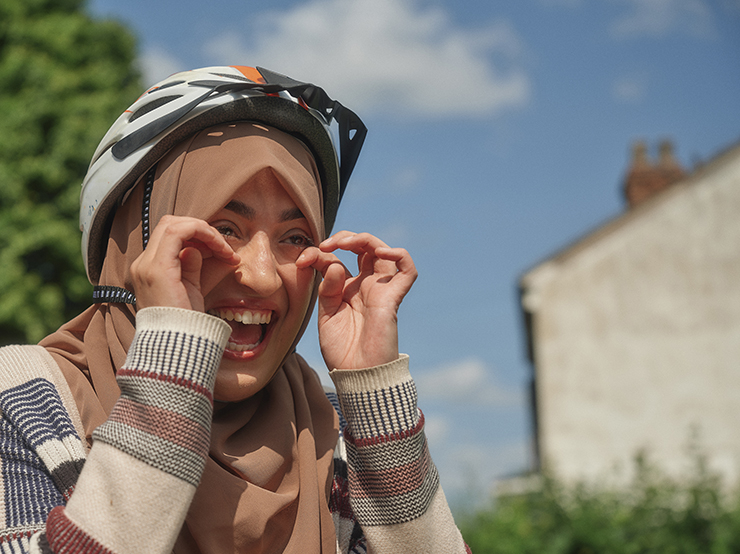 A woman wearing a headscarf and a bike helmet wipes happy tears away from her eyes while laughing