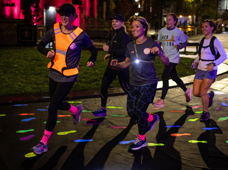 A group of women run at night down a road decorated with high-vis footprints.