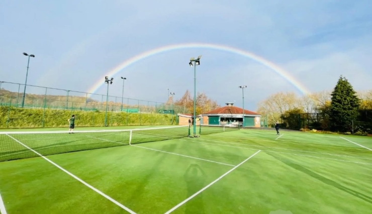 A rainbow arcs over a grass tennis court.