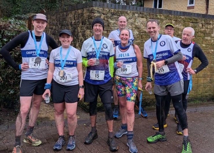 A group of runners from Chippenham Harriers pose for a photo in front of a wall, with medals around their necks.