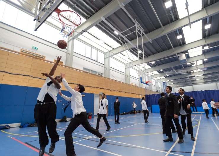 A group of schoolboys play basketball indoors