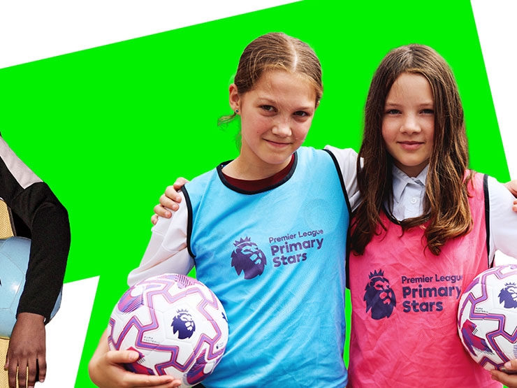Two girls, wearing high-vis training bibs, pose for a photo, arms around each other, each holding a football