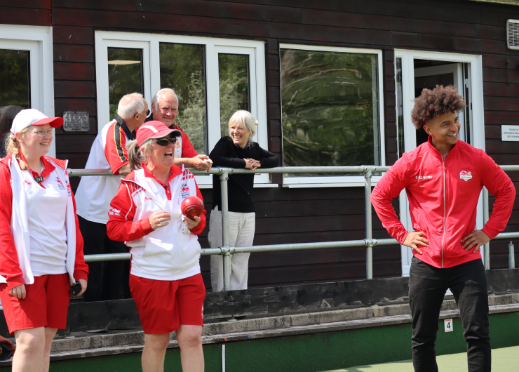 A group of bowlers wearing Team England kit laugh together on a green.