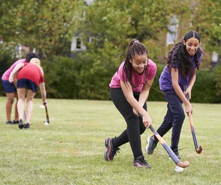  Two girls holding hockey sticks compete for the ball on a grass field.