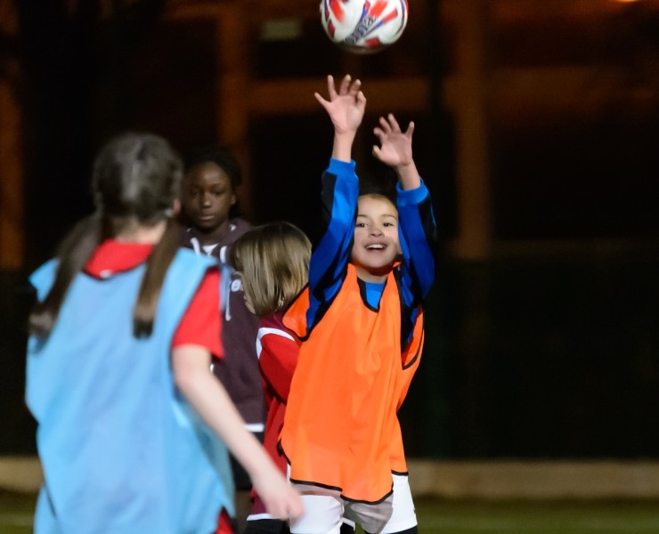 A smiling girl throws a football during a training session at night.