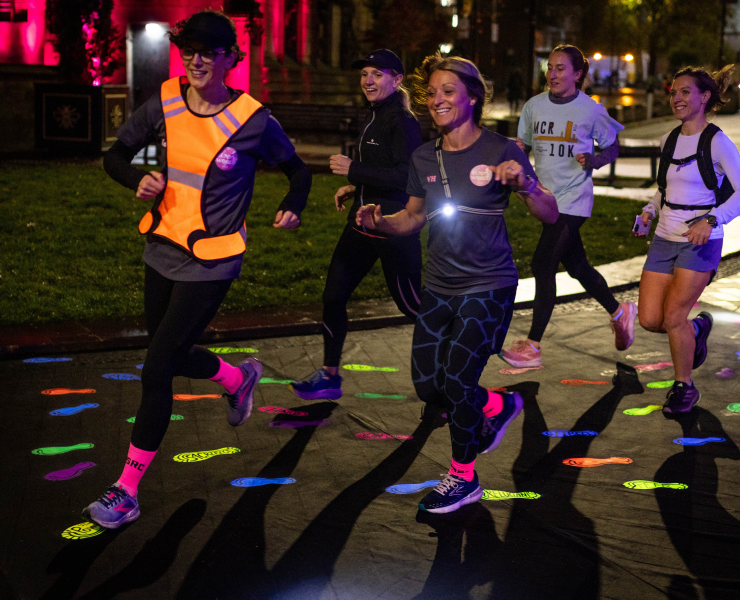 A group of women run at night down a road decorated with high-vis footprints.