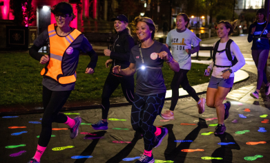 Women running over glow-in-the-dark footprints in a city at night