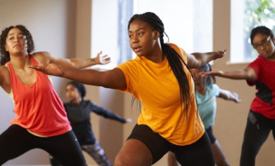 A group of women perform the warrior pose during a yoga class in a studio.